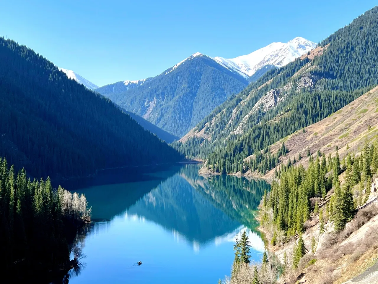 Tranquil waters of Kol Sai Lake surrounded by mountains.